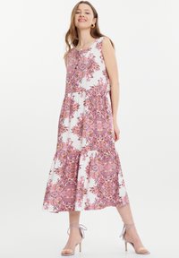 Blumenkleid in Weiß mit pinkem Paisleymuster, ärmelloses Design, lockere Passform und gestufter Saum. Kombiniert mit hellen High-Heels.