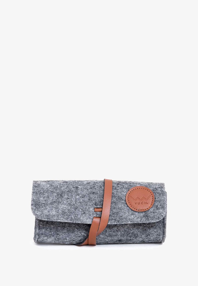 Šedá měkká peněženka s hnědým koženým páskem a kulatou nášivkou loga. Vyznačuje se překlopným designem a hladkým povrchem.