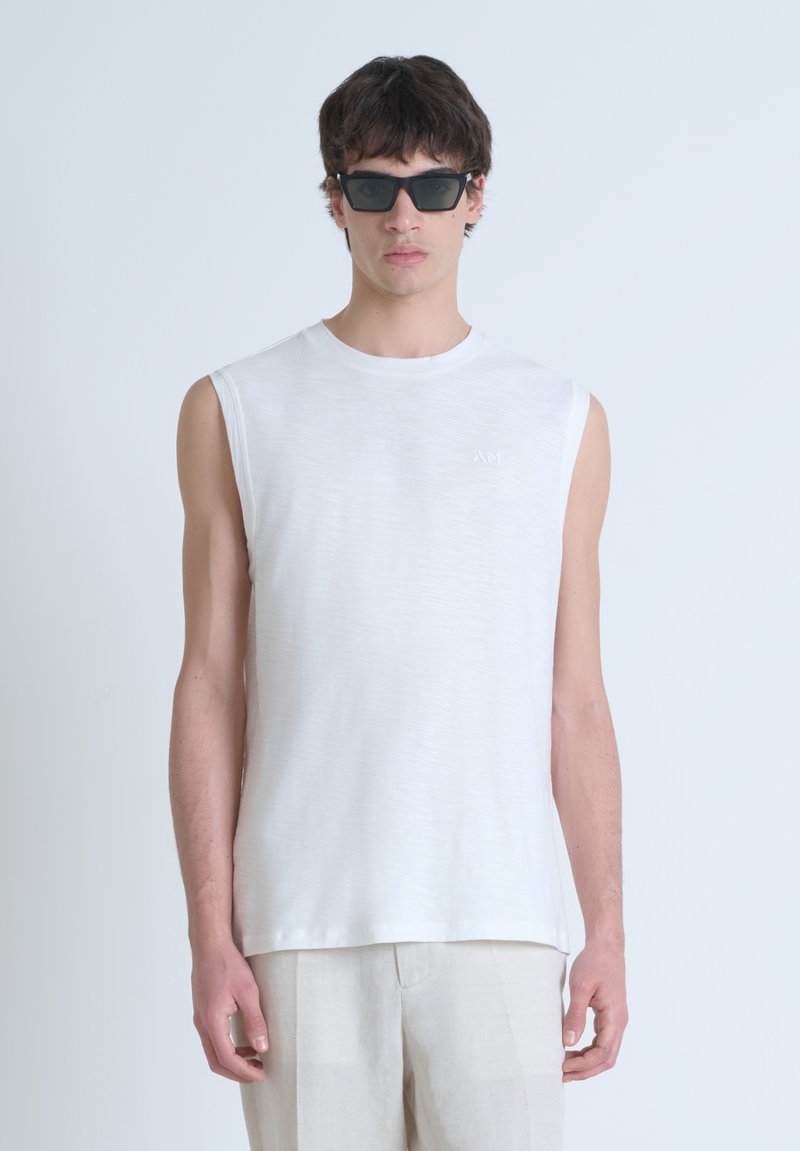 Camisa blanca sin mangas hecha de tejido ligero, con un cuello redondo y una textura sutil. Combinada con gafas de sol oscuras y de forma cuadrada.