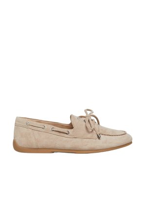 Beige suède loafer met veters, mocassinnaad, metalen oogjes en een platte rubberen zool, gezien van opzij tegen een witte achtergrond.
