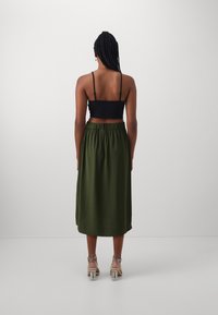 Schwarzes, tailliertes Trägertop und knielanger olivgrüner Rock mit elastischem Bund, kombiniert mit klaren Blockabsatzsandalen.