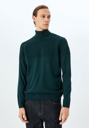 Suéter de cuello alto de canalé en azul verdoso oscuro, con un panel superior texturizado y una sección inferior lisa, mangas largas ajustadas y cintura elástica.