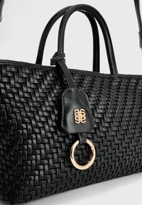 Zwarte geweven leren tas met twee handvatten, voorzien van een gouden ring en een geperst leren label. Glad textuur en ingewikkeld geweven patroon.