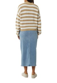 Gestreifter Pullover in Beige und Weiß, kombiniert mit einem hellblauen Jeansrock. Hat eine lockere Passform und einen runden Ausschnitt. Legere Schuhe sind zu sehen.