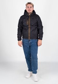 Czarna ocieplana kurtka z kapturem, z jasnopomarańczowymi akcentami na zamkach oraz dwoma przednimi kieszeniami, w połączeniu z niebieskimi dżinsami i białymi trampkami.