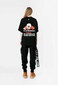 Camiseta negra de gran tamaño con un gráfico de dibujos animados y texto en la parte de atrás, combinada con pantalones cargo negros y botas de tobillo color beige con una suela gruesa.