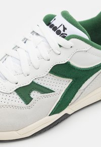 Sneaker with a green suede accent and white leather upper, featuring perforated details and white laces, rubber sole, and branding on tongue.
