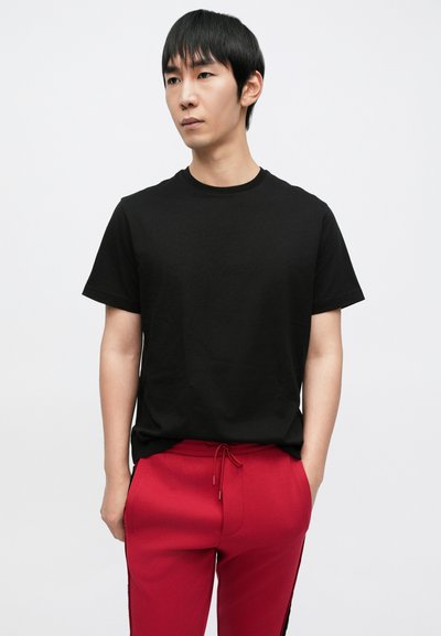 Musta puuvillainen T-paita, jossa on lyhyet hihat ja pyöreä pääntie, yhdistetty punaisiin, sivuraidoilla varustettuihin narupantaiseen housuihin.