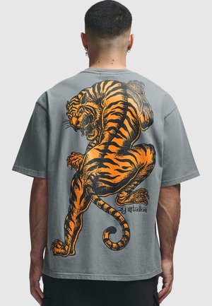 Camiseta gris de gran tamaño con un gran gráfico de un tigre naranja en la parte posterior. Mangas cortas, ajuste relajado y textura de tela suave.