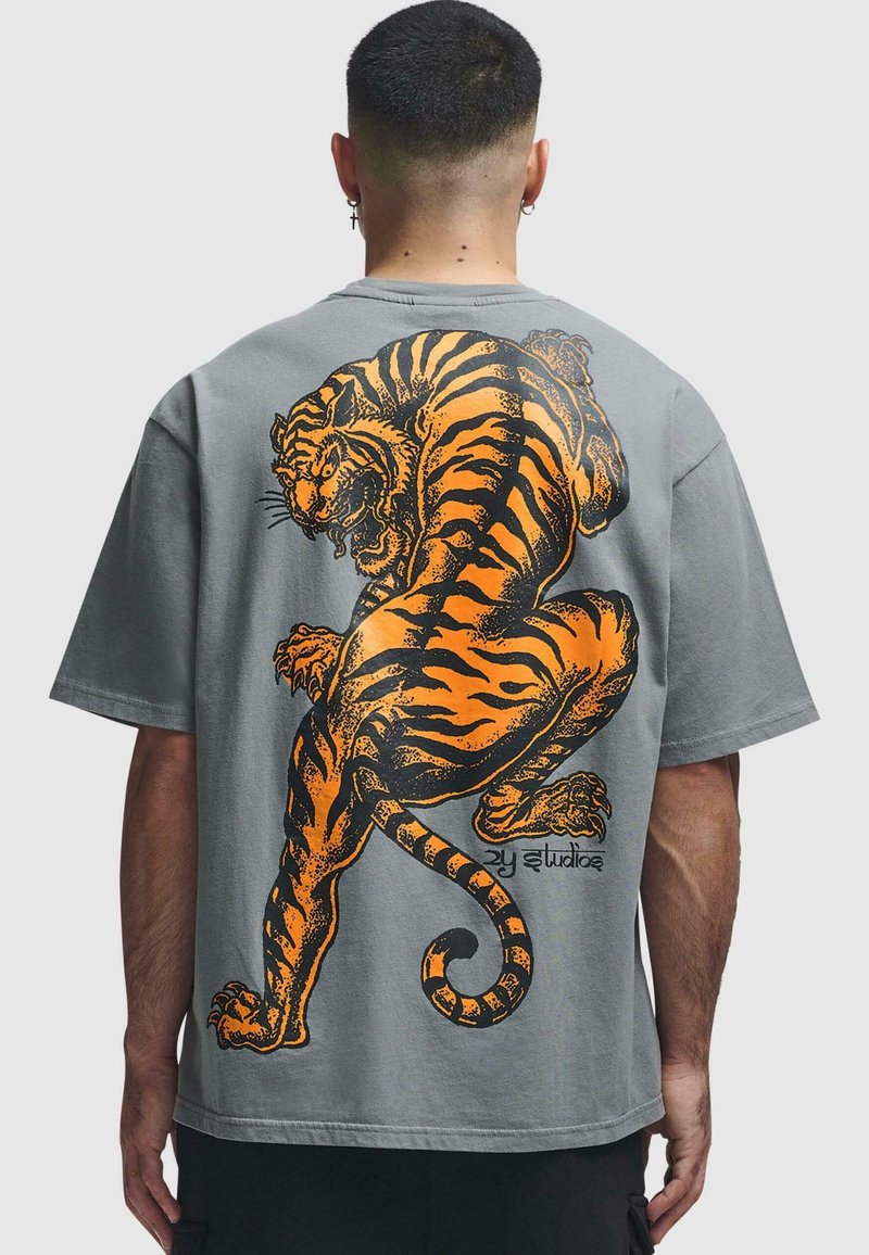 Grå oversized t-skjorte med et stort oransje tiger-design på baksiden. Korte ermer, avslappet passform og myk stofftekstur.