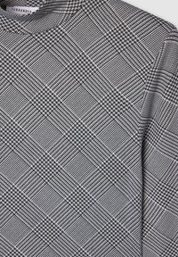 Top a maniche lunghe a scacchi houndstooth bianco e nero con scollatura rotonda, con etichetta del marchio Terranova all'interno del colletto.
