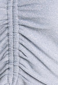 Lichtblauwe stof met een glinsterende textuur, voorzien van geplooide plooien langs het midden en een zachte, slinkse uitstraling.
