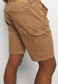 Shorts cargo marron en tissu de coton robuste, avec plusieurs poches latérales et arrière, coupe droite et ourlets retroussés.