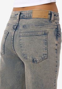 Sieviete valkā augsta vidukļa gaiši mazgātas džinsa bikses ar redzamām aizmugures kabatām un brūnu ādas etiķeti ar uzrakstu "NOISY MAY".