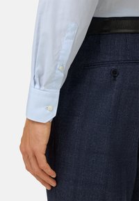 Světle modrá kostkovaná košile s manžetami na knoflíky, kombinovaná s tmavě modrými texturovanými kalhotami s jemným kostkovaným vzorem.