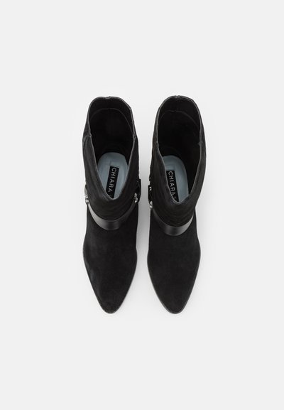 Black suede ankle boots with pointed toes, featuring a wide black leather strap and a decorative silver accent on the side.