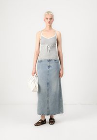 Débardeur gris à côtes avec ourlet en dentelle, taille cintrée, associé à une longue jupe en denim bleu, des chaussures à imprimé léopard et un sac blanc.