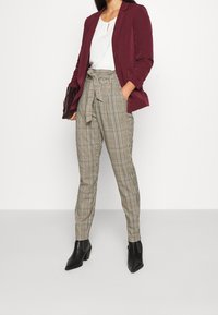 Kastanjefärgad kavaj över en vit blus; hög midja, rutiga byxor; svarta ankelboots; slät tyg, skräddarsydd passform och knytdetalj i midjan.