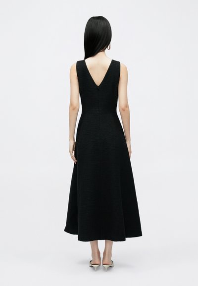 Melnas maksikleita ar teksturētu audumu, bez piedurknēm un V veida muguras detaļu. Sasniedz potītes, kombinēta ar augstpapēžu kurpēm ar smailu purngalu.