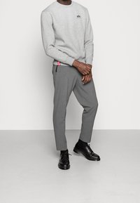 Felpa grigia con scollo rotondo e piccolo logo, abbinata a pantaloni grigi sartoriali e scarpe nere. Design minimalista, tessuto testurizzato.