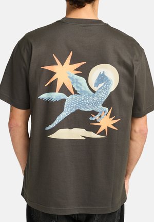 T-shirt gris foncé à manches courtes arborant un design de créature ailée bleue, avec des étoiles orange clair et un halo pâle dans le dos.