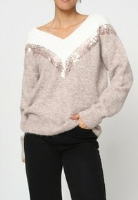 Pull en laine beige clair avec un décollet é en V blanc et un motif diagonale de sequins rose doré pailletés sur la poitrine et les épaules.