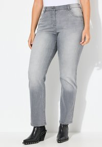 Jeans in denim grigio con taglio dritto, dotati di tasche posteriori e chiusura con bottone. Indossati con stivaletti neri alla caviglia con borchie argentate.