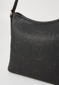 Sac à main en cuir noir avec des motifs floraux et de logo en relief, une forme arrondie, une surface texturée et une attache pour bandoulière.
