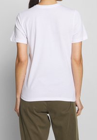 Camiseta de algodón blanca con mangas cortas, cuello redondo y una textura suave. La camiseta está combinada con pantalones caquis.
