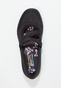 Zapato de punto negro con dos tiras elásticas. La plantilla de espuma con memoria presenta un patrón floral. Diseño ligero y flexible.