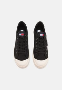 Svarte kanvas sneakers med hvit gummi tåhette, med svarte snørebånd og en logomerking på siden. Myk tekstur og lavprofil-design.
