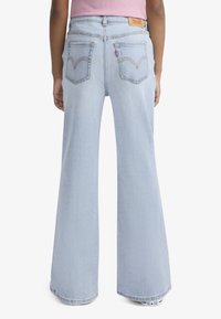 Šviesiai melsvos kelnės iš džinso su plačiomis kojomis, aukštu liemeniu, dviem kišenėmis gale ir subtiliais geltonais siūlais.