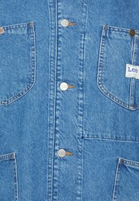Modrá džínová košile se stříbrnými patkami, dvěma předními kapsami a štítkem s logem Lee. Má klasický střih a hladkou, strukturovanou látku.