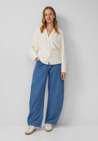 Crème knopjesoverhemd met lange mouwen, gecombineerd met wijde blauwe denim jeans en witte sneakers met tan accenten. Eenvoudige, ontspannen pasvorm.