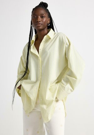 Gul og hvid stribet oversized skjorte med knaplukket krave og lange ærmer. Blødt stof med afslappet pasform og sidelommer.
