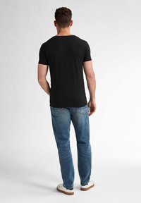 Tricou negru cu mânecă scurtă, confecționat dintr-un material moale, asociat cu blugi albastre deschise. Ghetele sunt albe cu talpă maro deschis.