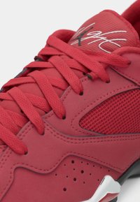 Zapatilla deportiva roja con cordones a juego, panel lateral de malla, detalles perforados y logo blanco en la lengüeta acolchada.