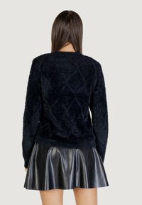 Pull en velours bleu marine avec un motif en losange, doté de manches longues et d'un col rond, associé à une jupe évasée en cuir noir.