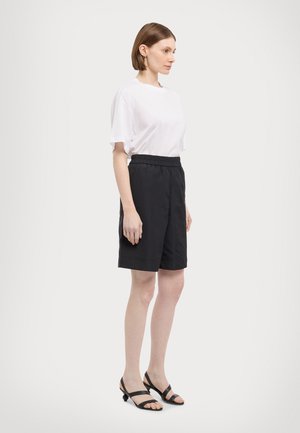 Witte katoenen t-shirt en zwarte shorts met elastische tailleband. De outfit omvat zwarte sandalen met straps, met een relaxte pasvorm en een gladde textuur.