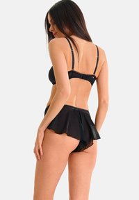 Soutien-gorge noir avec des accents transparents et des bretelles réglables, assorti à un short noir à volants avec un design fluide. Tissu texturé visible.