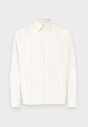 Chemise blanche à manches longues avec des rayures verticales subtiles et un col pointu, posée à plat sur un fond clair.