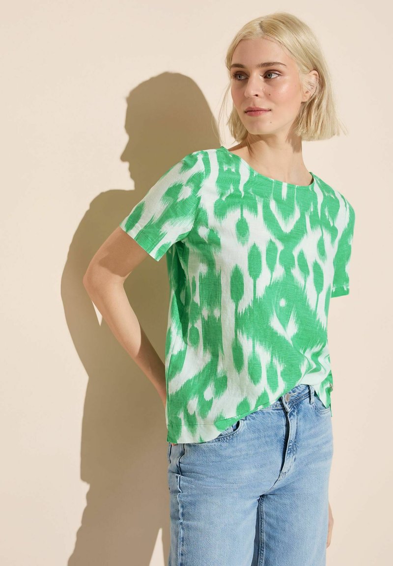 Top corto a maniche corte verde e bianco con scollatura rotonda. Realizzato in tessuto leggero, presenta un design astratto in stile tie-dye.