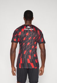 Čierny a červený športový dres s geometrickým vzorom. Na zadnej strane v oblasti krku je bielym písmom nápis "OGC NICE".