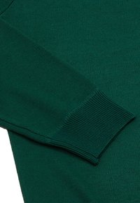 Mâneca unui pulover tricotat de culoare verde închis, cu manșete ribbate și o textură netedă. Materialul are un model de țesătură uniform pe toată suprafața.