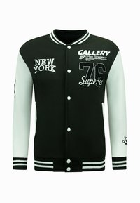 Zwart-witte varsity jack met geborduurde tekst, knopen en gestreepte ribbels. Heeft ontwerpen van "NEW YORK" en "76". Gladde textuur.