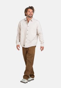 Light beige button-up shirt with long sleeves, paired with brown pants and gray sneakers, featuring a relaxed fit and casual style.
