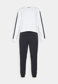 Λευκή μπλούζα με μαύρες ρίγες στις μανσέτες και σκούρο γκρι φόρμες, διαθέτοντας άνετη εφαρμογή και ελαστικές μανσέτες στους αστραγάλους.