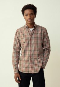 Camicia a quadri nei colori beige, rosso e verde. Presenta maniche lunghe, colletto con bottoni e una tasca sul petto. Tessuto di cotone liscio.