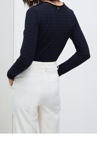 Marynarski pasiasty longsleeve z okrągłym dekoltem i detalami z guzikami z tyłu, zestawiony z białymi, prążkowanymi spodniami o wysokim stanie.