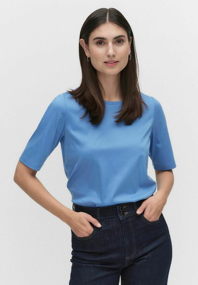 Blå kortärmad topp av slät tyg, med rund halsringning och en avslappnad passform, ihop med höga, mörka denimjeans.